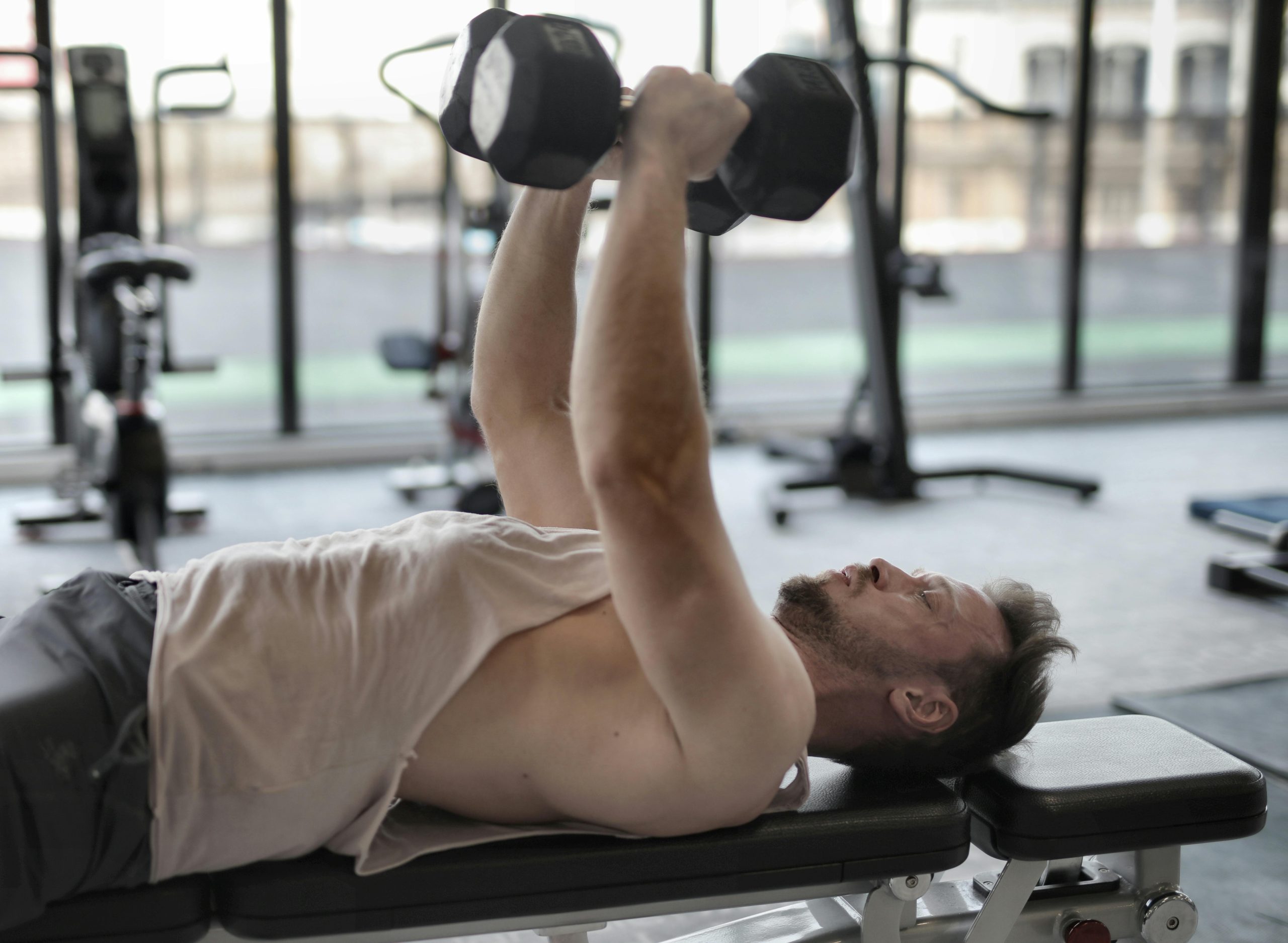 Man performing dumbbell press on bench indoors, focusing on muscle strength.