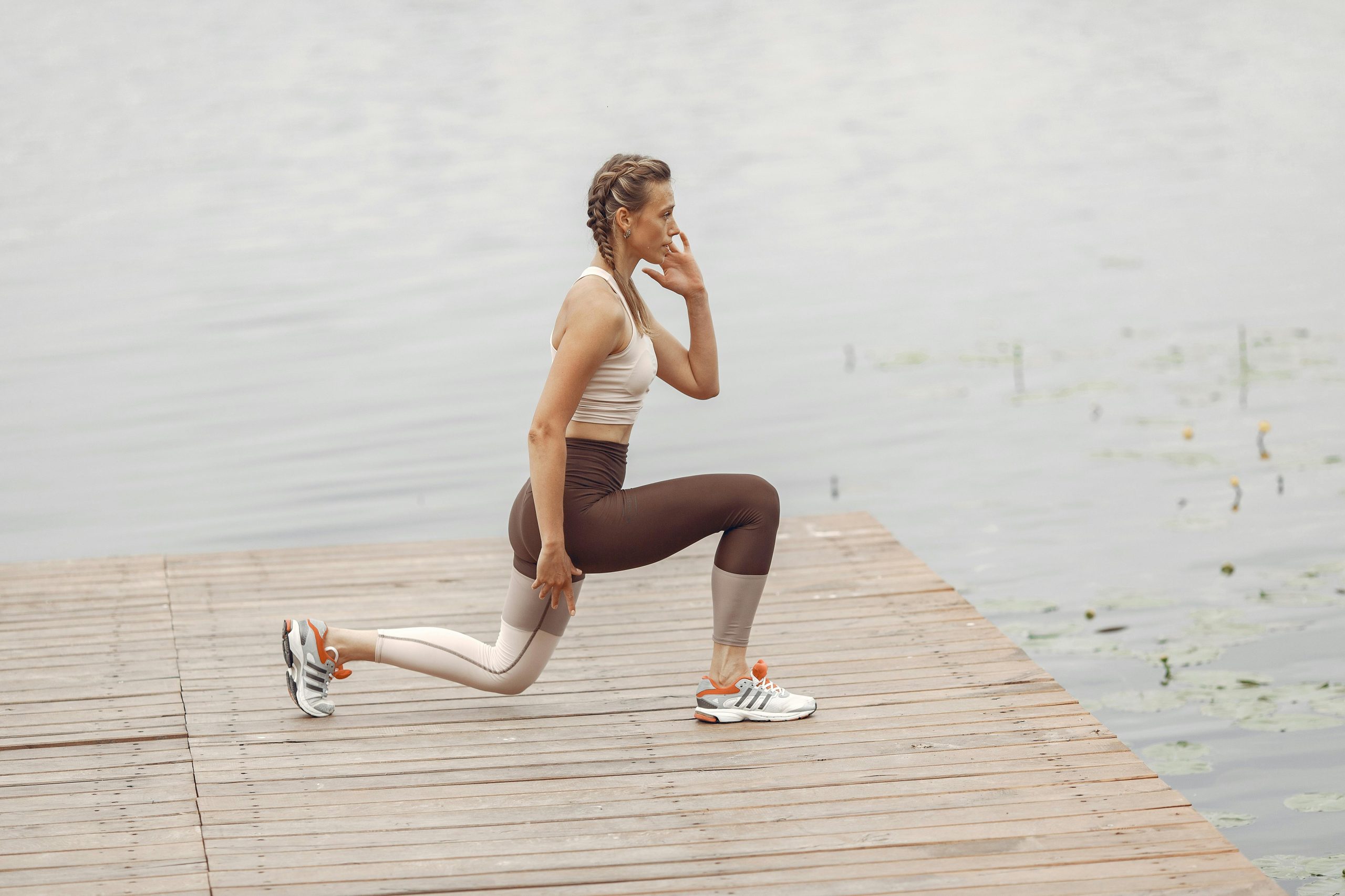 A woman performs lunges on a lakeside wooden deck, showcasing a fit lifestyle outdoors.