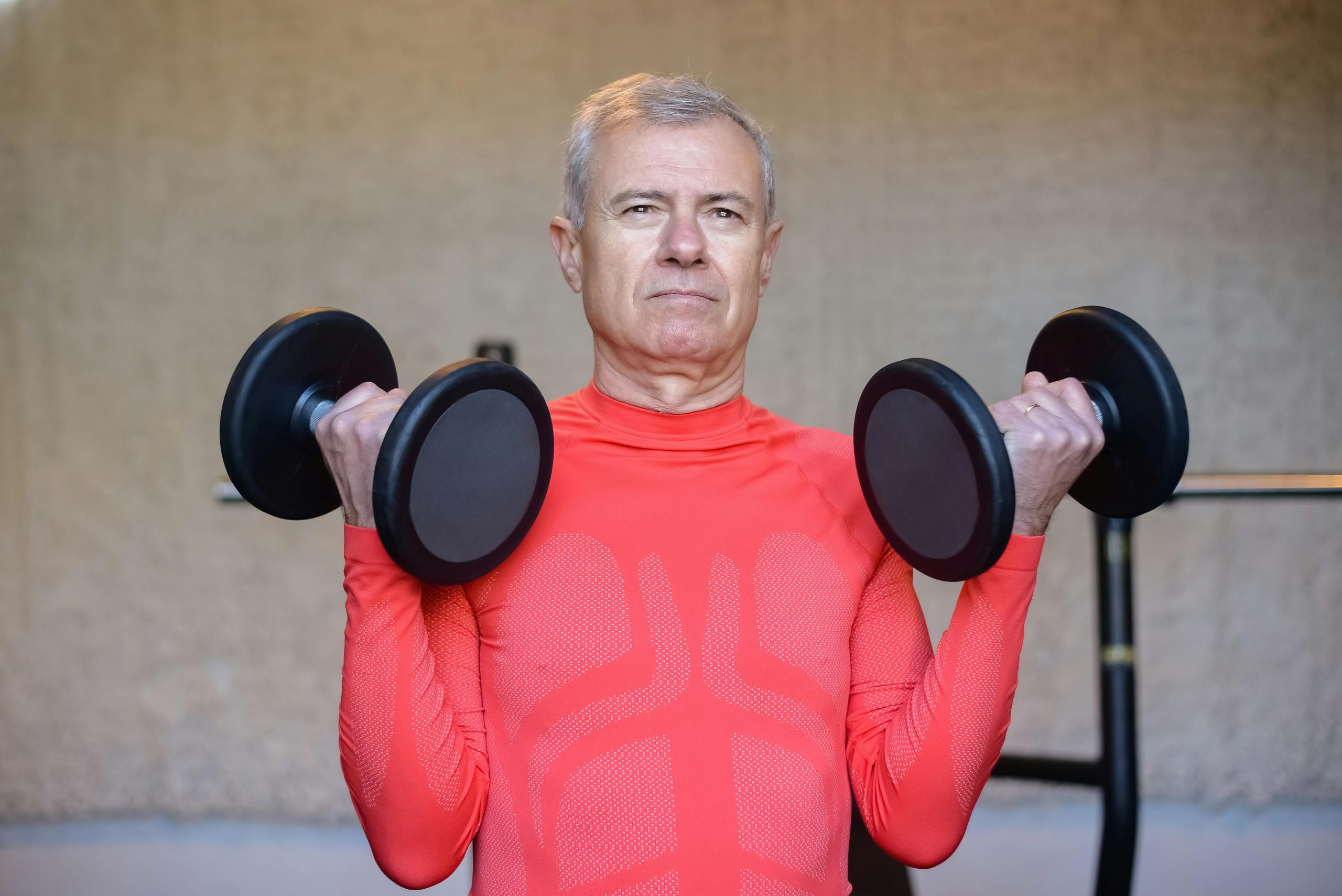 Elderly man in red lifting dumbbells, promoting fitness and healthy aging indoors.