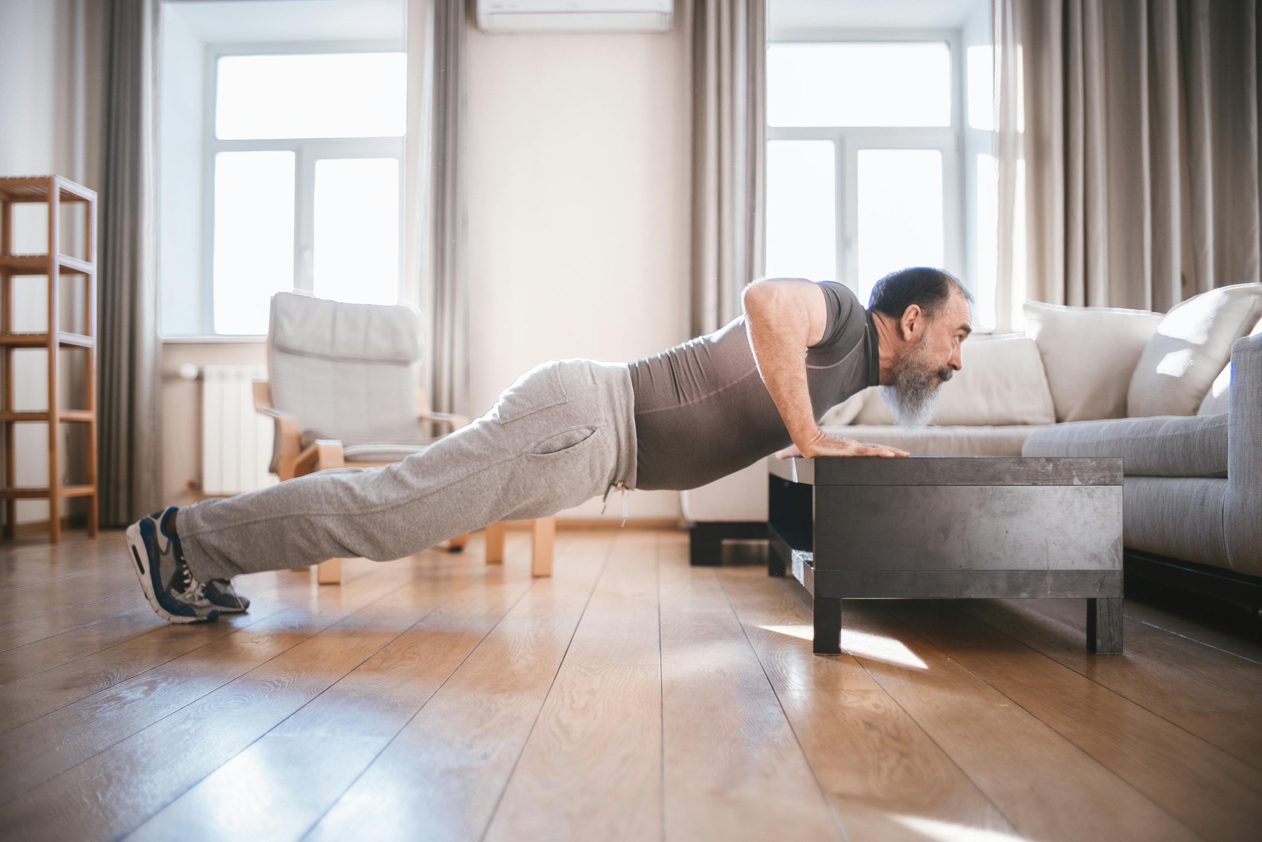 Senior man exercising at home with push-ups on a wooden floor, promoting healthy lifestyle.